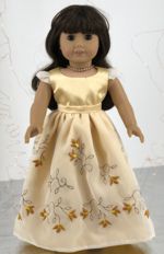 A doll in a pale yellow skirt with embroidered overlay and a top.