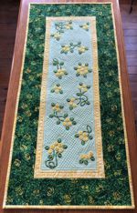 A quilted tablerunner with embroidered flowers in yellow and green tones