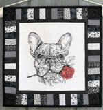 A small black and white wall quilt with embroidery of a French Bulldog with a red rose.