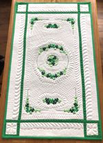 Light-colored quilted tablerunner with green borders and shamrock embroidery