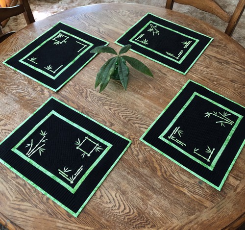 4 black placemats with neon green embroidery of bamboo stems and leaves on a table