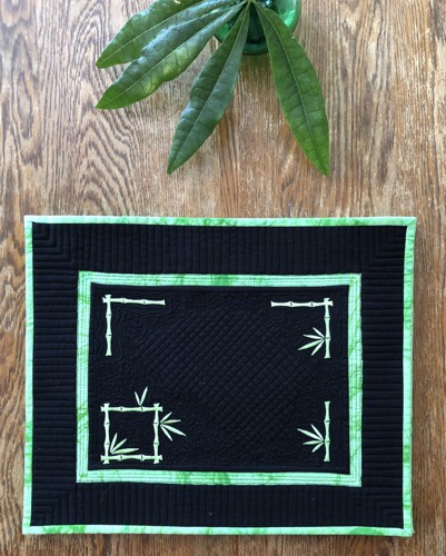 A black quilted placemat with bamboo embroidery in neon green color