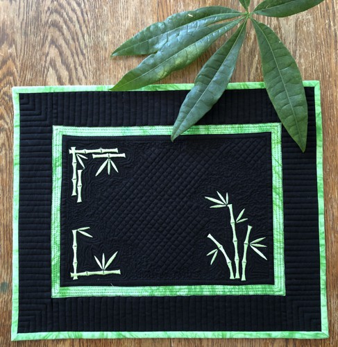 A black quilted placemat with bamboo embroidery in neon green color