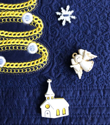 A close-up of the quilt with snowflake, deer, Santa's sleigh, church, and angel buttons