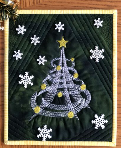 A small quilt with embroidered Christmas tree on a dark green background, decorated with snowflake buttons.