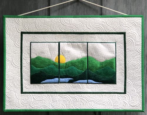 A small quilt with embroidered mountain landscape.