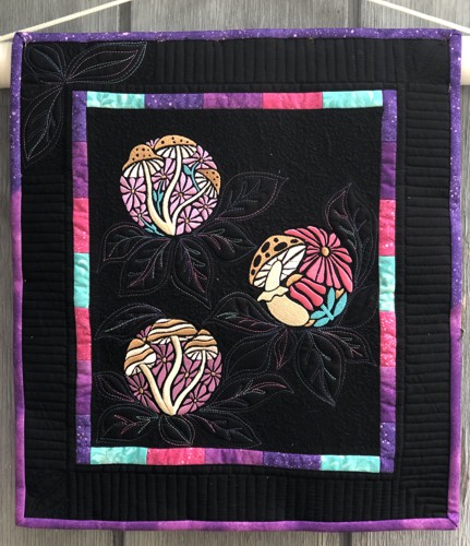 A small black quilt with embroidered flowers and mushrooms in jewell tones
