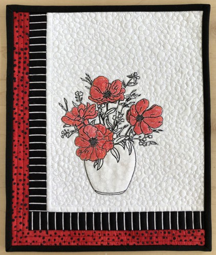 A small wall quilt with an embroidery of poppies in the center