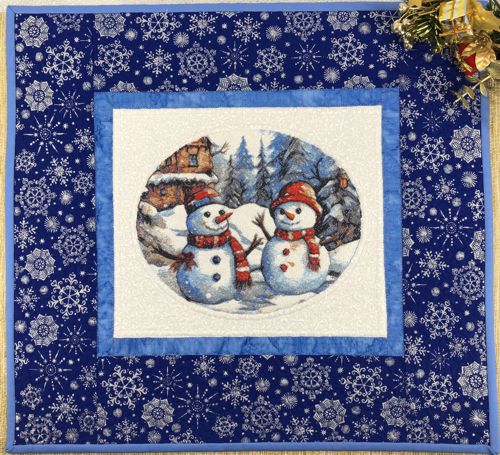 A small blue-and-white quilt with embroidered snowmen in the center.