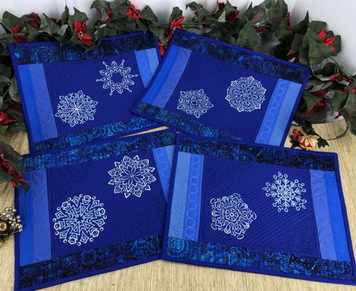 Four quilted placemats in blue hues with snowflake embroidery