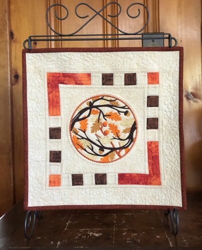 A quilt with embroidery of fall branches in the center.