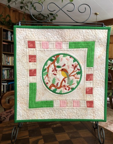 A quilt with embroidery of spring branches and a bird in the center.