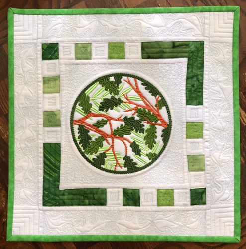 A quilt with embroidery of summer branches in the center.