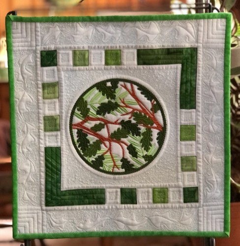 A quilt with embroidery of summer branches in the center.