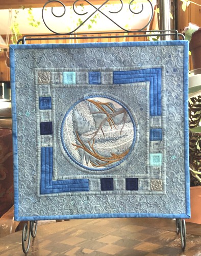 A quilt with embroidery of winter branches in the center.