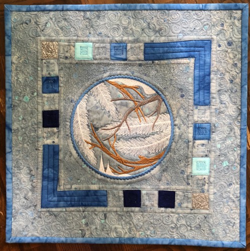 A quilt with embroidery of winter branches in the center.