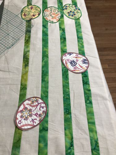 Paper templates of the embroidery designs pinned to the quilter's top.