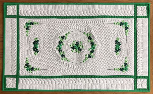 Light-colored tablerunner with green borders and shamrock embroidery.